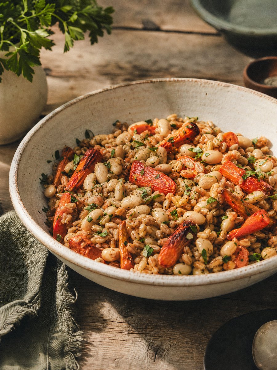 A wide ceramic bowl filled with cooked farro, whole white beans, and roasted carrot pieces, dressed lightly with oil and herbs.